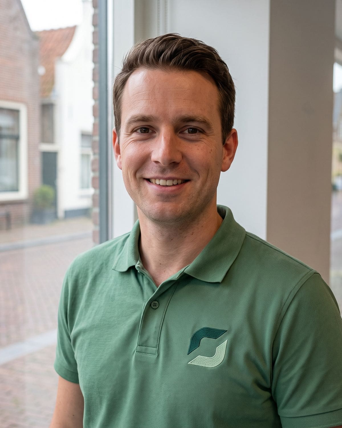 Medewerker van Duurzaam Opgelost in een polo met het logo, bij het raam van het kantoor